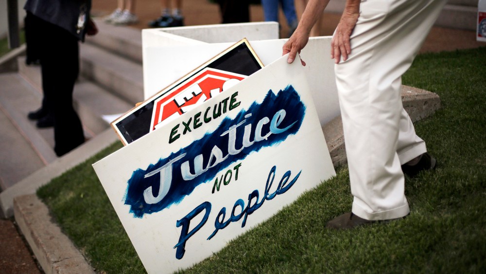 A death penalty opponent picks up a sign hours before the scheduled execution of a Missouri death row inmate, May 20, 2014, in St. Louis.