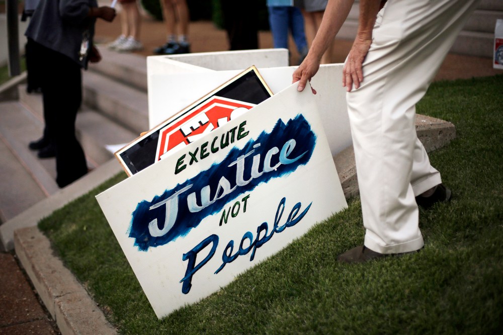 A death penalty opponent picks up a sign hours before the scheduled execution of a Missouri death row inmate, May 20, 2014, in St. Louis.