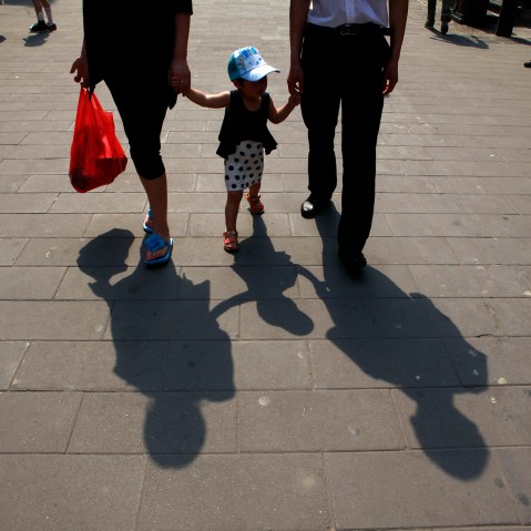 A couple hold hands with a child along a retail street in Beijing, China. (Photo by Ng Han Guan/AP)
