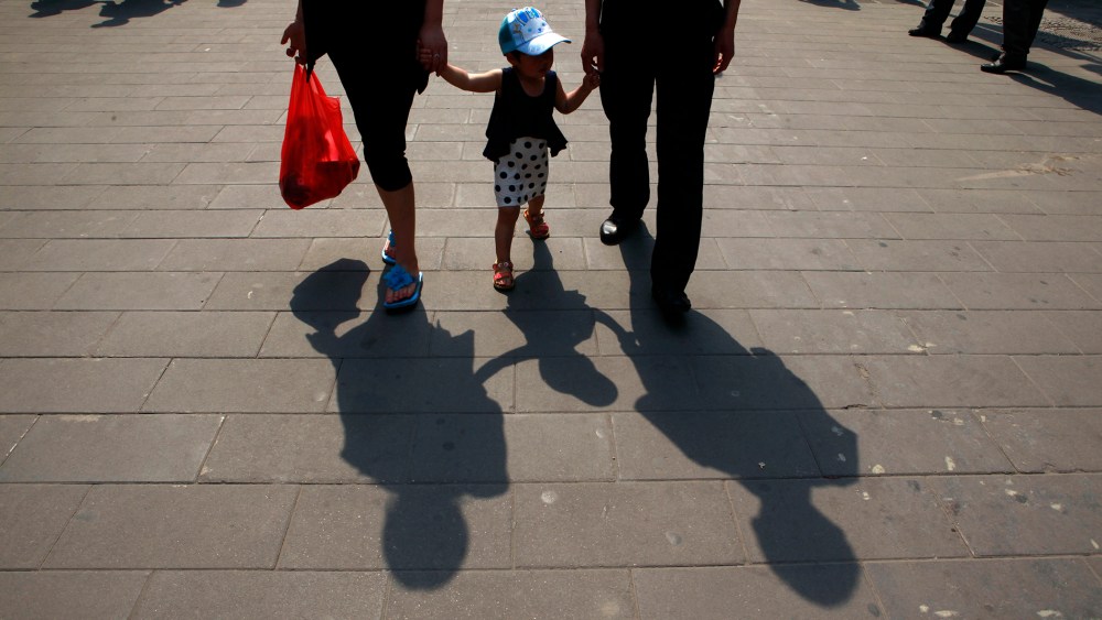 A couple hold hands with a child along a retail street in Beijing, China. (Photo by Ng Han Guan/AP)