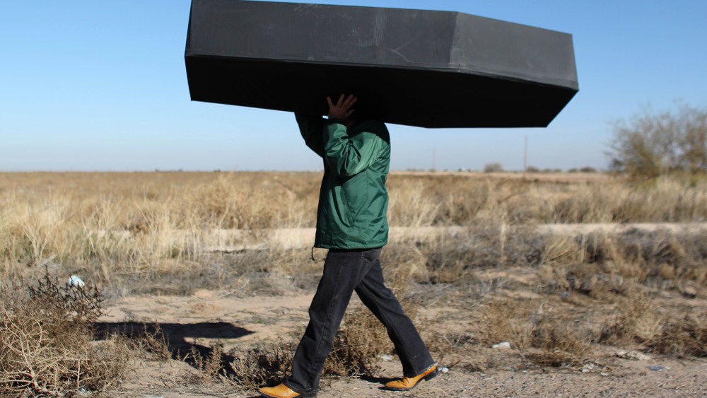 In this Jan. 20, 2016 file photo, a demonstrator carries a mock coffin, representing migrants who have died, outside the U.S. Immigration and Customs Enforcement detention center in Eloy, Ariz. (Photo by Ricardo Arduengo/AP)