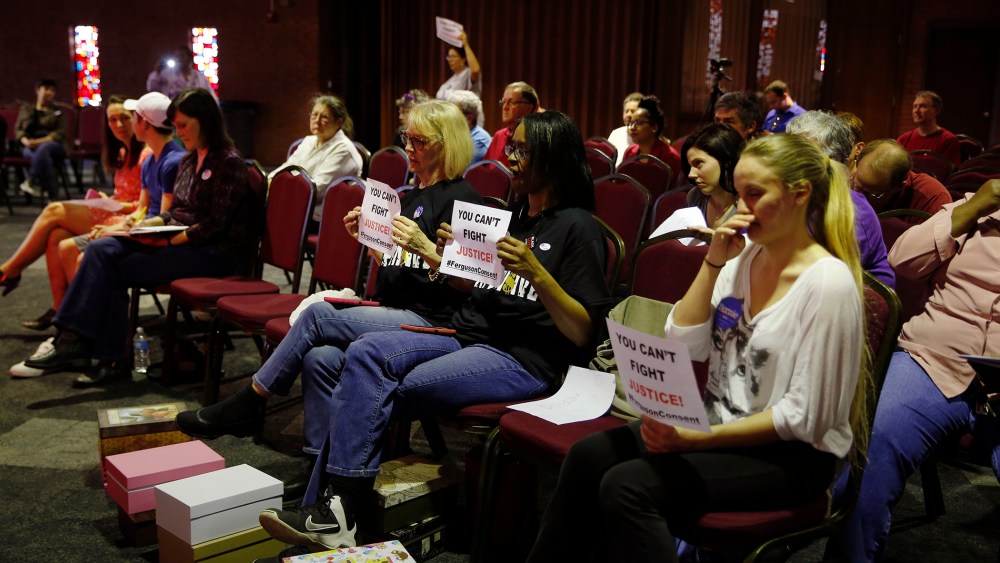 In this March 15, 2016 file photo, people watch and hold signs as members of the Ferguson City Council meet in Ferguson, Mo. (Photo by Jeff Roberson/AP)