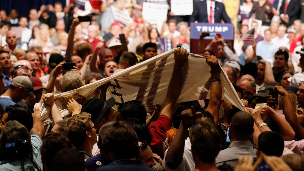 Trump supporters pull down an immigration rights protest banner as Trump speaks in the background, Saturday, July 11, 2015, in Phoenix, AZ. (Photo by Ross D. Franklin/AP)
