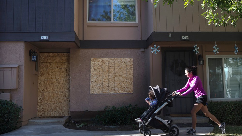 A woman pushes a baby stroller past the boarded-up townhouse rented by San Bernardino shooting rampage suspects Syed Farook and his wife, Tashfeen Malik, Saturday, Dec. 5, 2015, in Redlands, Calif. (Photo by Jae C. Hong/AP)