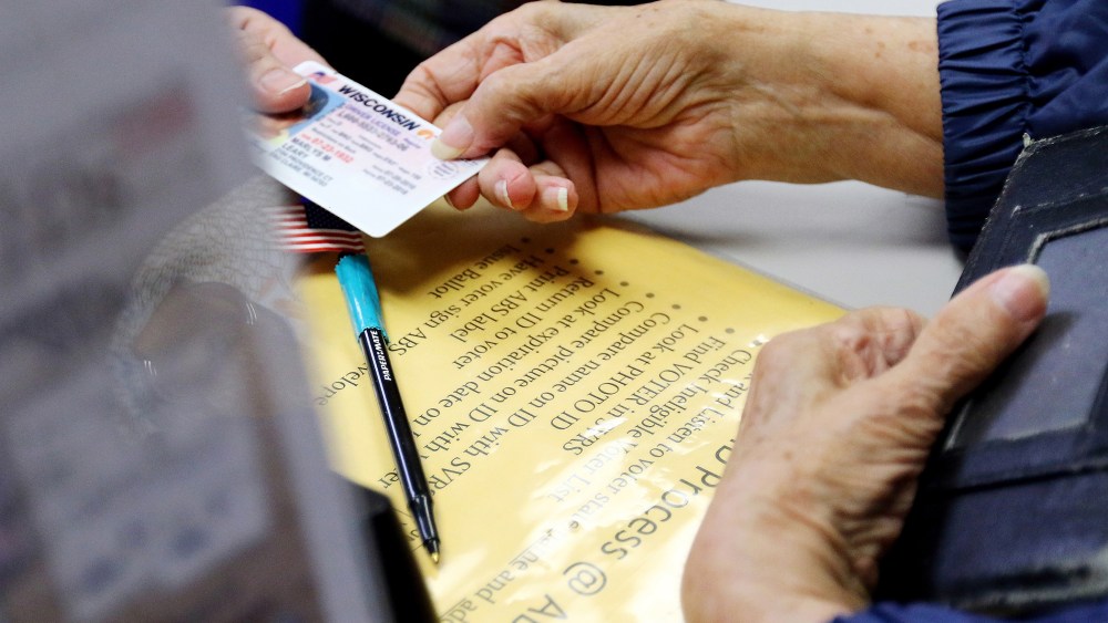 A voter in Eau Claire, Wis. hands her photo identification card to an election assistant on March 21, 2016, at the City of Eau Claire Elections Office. (Photo by Marisa Wojcik/The Eau Claire Leader-Telegram/AP)