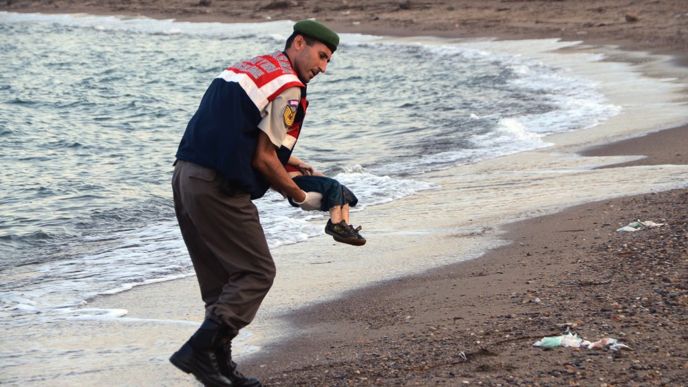 A paramilitary police officer carries the lifeless body of a migrant child near the Turkish resort of Bodrum early Wednesday, Sept. 2, 2015. (Photo by DHA/AP)