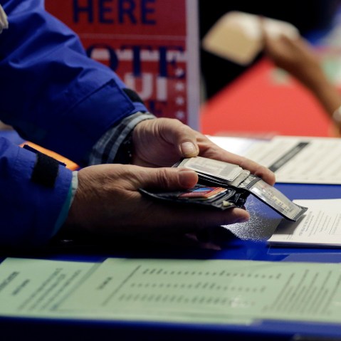 A voter shows his photo identification to an election official at an early voting polling site, in Austin, Texas on Feb. 26, 2014. (Photo by Eric Gay/AP)