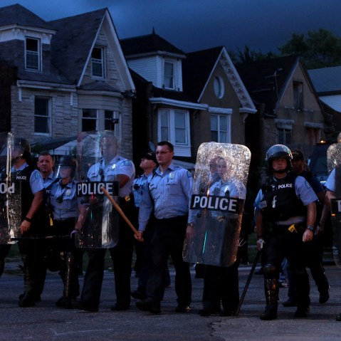 Police stand guard as protesters gather, Aug. 19, 2015, in St. Louis after a black 18-year-old fleeing from officers serving a search warrant was fatally shot after police say he pointed a gun at them. (Photo by Laurie Skrivan/St. Louis Post-Dispatch/AP)