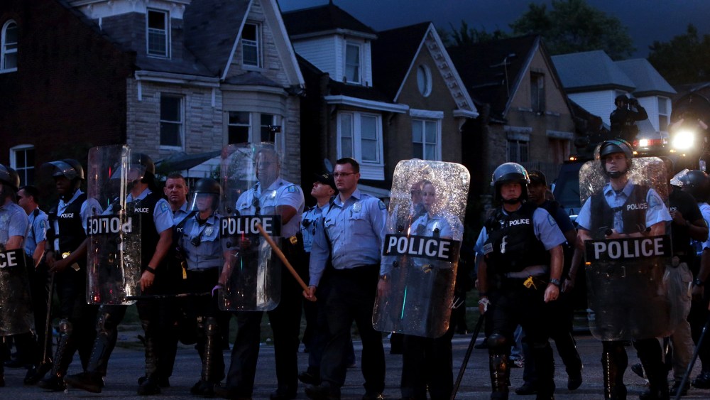 Police stand guard as protesters gather, Aug. 19, 2015, in St. Louis after a black 18-year-old fleeing from officers serving a search warrant was fatally shot after police say he pointed a gun at them. (Photo by Laurie Skrivan/St. Louis Post-Dispatch/AP)