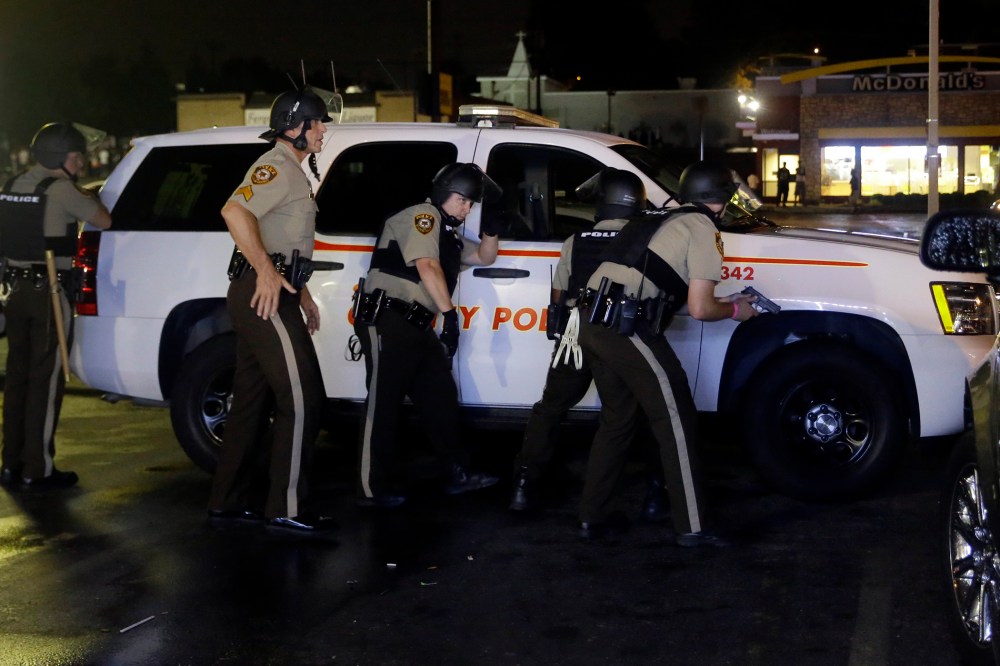 Members of the St. Louis County Police Department take cover at a protest in Ferguson, Mo., Aug. 9, 2015. (Photo by Jeff Roberson/AP)