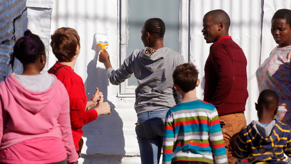 A woman, center, paints a shack with white fire retardant paint as part of their contribution to International Nelson Mandela Day in the township of Nomzamo, South Africa on July 18, 2015. (Photo by Schalk van Zuydam/AP)