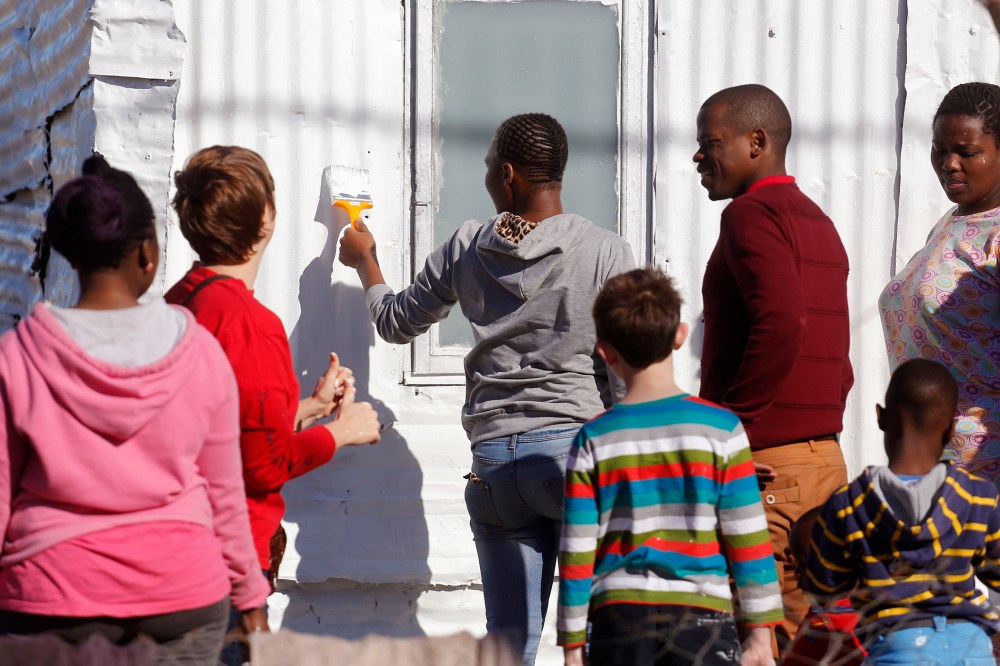 A woman, center, paints a shack with white fire retardant paint as part of their contribution to International Nelson Mandela Day in the township of Nomzamo, South Africa on July 18, 2015. (Photo by Schalk van Zuydam/AP)