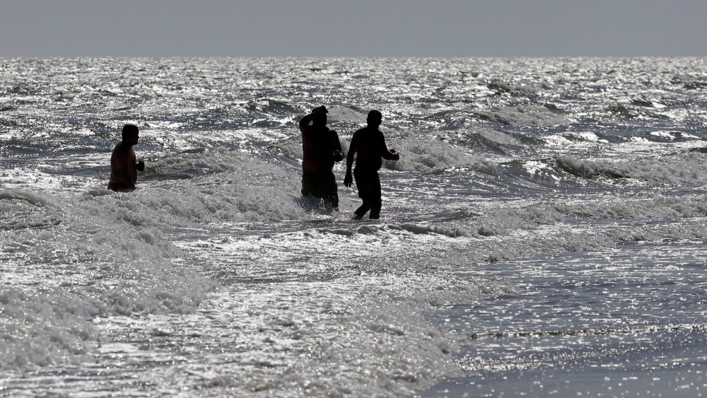 Vacationers walk in the surf in Oak Island, N.C. on June 15, 2015, the day after two separate shark attacks. (Photo by Chuck Burton/AP)