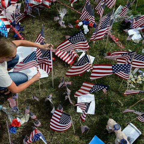 A mourner places an American flag by a makeshift memorial outside the Armed Forces Career Center in Chattanooga, Tenn. on Jul. 20, 2015 (Photo by Mark Zaleski/AP).