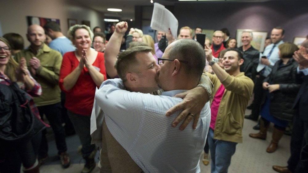 Chris Serrano, left, and Clifton Webb kiss after being married, as people wait in line to get licenses outside of the marriage division of the Salt Lake County Clerk's Office in Salt Lake City, Friday, Dec. 20, 2013.