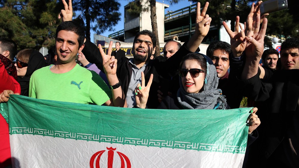 Iranians flash the victory sign as they hold their country's flag while waiting for arrival of Foreign Minister Mohammad Javad Zarif from Lausanne, Switzerland, at the Mehrabad airport in Tehran, Iran, April 3, 2015. (Photo by Ebrahim Noroozi/AP)
