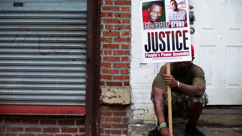 A demonstrator holds a sign bearing the likeness of Eric Garner and Michael Brown before a march to protest the death of Garner, Aug. 23, 2014, in the Staten Island borough of New York, N.Y
