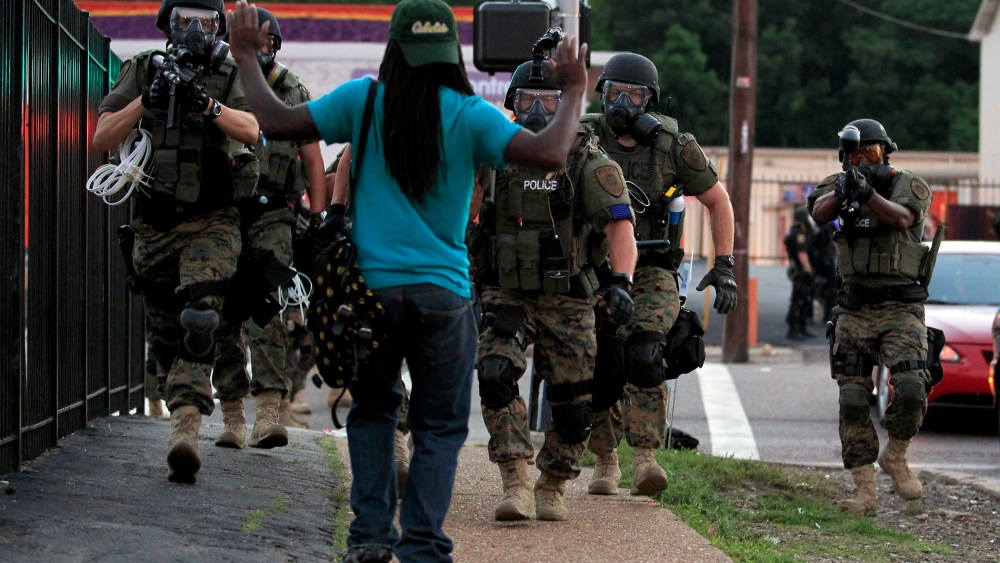 Police wearing riot gear walk toward a man with his hands raised Monday, Aug. 11, 2014, in Ferguson, Mo.