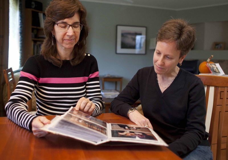 In this photo taken Nov. 12, 2012, Karen Golinski (left) and Amy Cunninghis look over a photo album of their wedding photos in San Francisco. Golinski wanted to enroll her spouse in her employer-sponsored health plan. Four years later, her request...