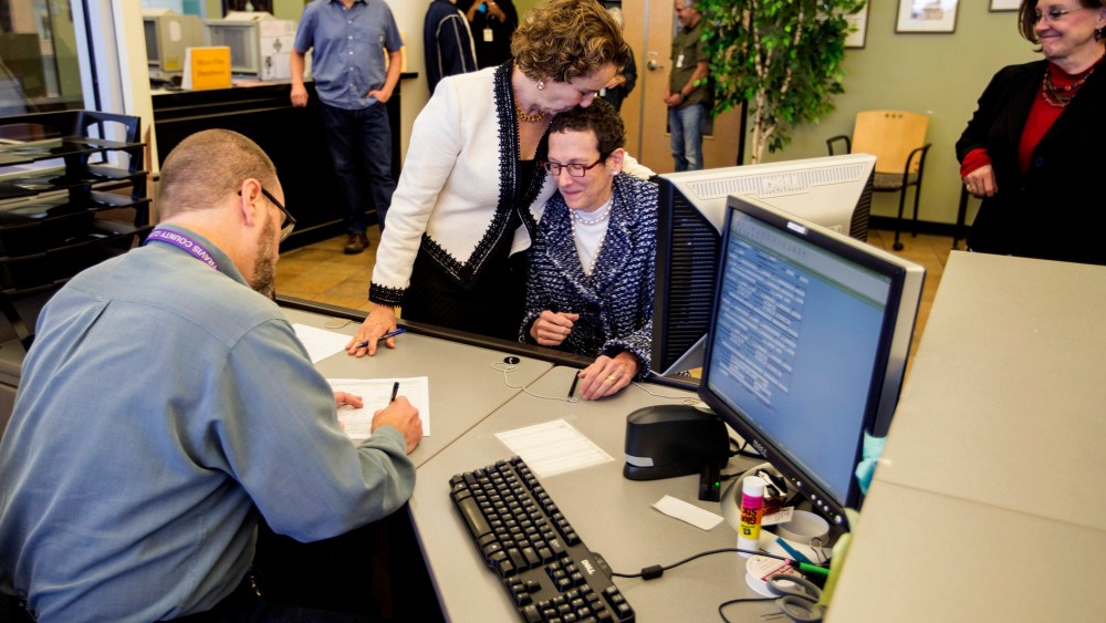Suzanne Bryant, left, and Sarah Goodfreind hug as recording specialist Michael Mitchell for the Travis county clerk's office records the final paper work of their marriage certificate. (Photo by Ricardo B. Brazziell/Austin American-Statesman/AP)