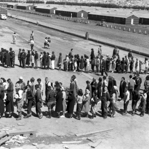 Newly arrived Japanese evacuees line up outside a mess hall at the Tanforan Assembly Center, in San Bruno, Ca., April 29, 1942. (Photo by Dorothea Lange/Interim Archives/Getty)