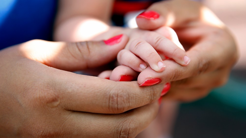A young girl grasps the hand of her newborn daughter. (Photo by Marc Piscotty/The Washington Post/Getty)