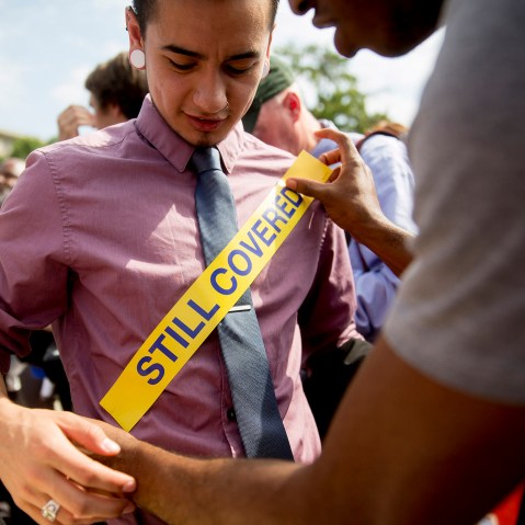 Demonstrator Ron Busby, with Center for American Progress, right, places a "Still Covered" sticker onto Kory Masen after the U.S. Supreme Court ruled 6-3 to save Obamacare tax subsidies, June 25, 2015. (Photo by Andrew Harrer/Bloomberg/Getty)