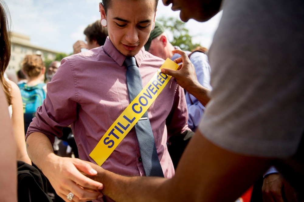 Demonstrator Ron Busby, with Center for American Progress, right, places a "Still Covered" sticker onto Kory Masen after the U.S. Supreme Court ruled 6-3 to save Obamacare tax subsidies, June 25, 2015. (Photo by Andrew Harrer/Bloomberg/Getty)