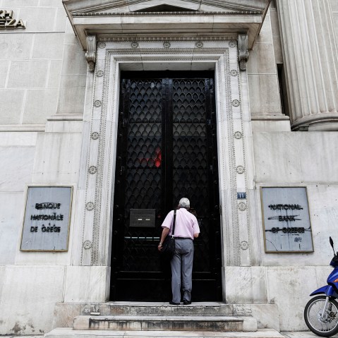 A pedestrian pauses to look through the closed doors of a National Bank of Greece SA bank branch before opening in Thessaloniki, Greece, on June 29, 2015. (Photo by Konstantinos Tsakalidis/Bloomberg/Getty)
