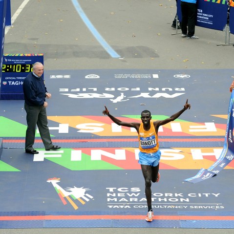 Stanley Biwott of Kenya crosses the finish line to win the Pro Men's division in the NYC Marathon. Police Commissioner William J. Bratton and marathon Grand Marshal Spike Lee hold up the finish ribbon, Nov. 1, 2015. (Photo by Craig Barritt/Getty)