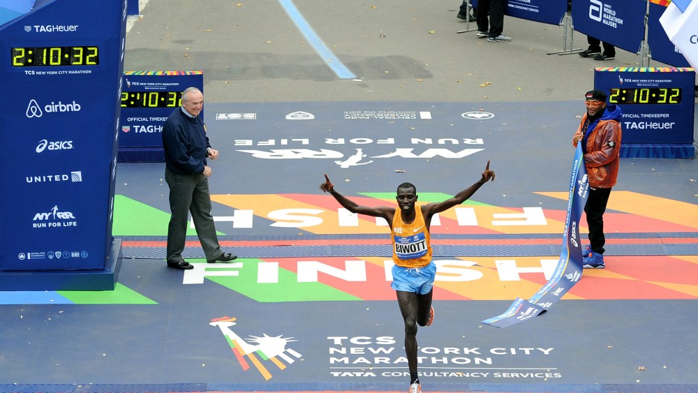 Stanley Biwott of Kenya crosses the finish line to win the Pro Men's division in the NYC Marathon. Police Commissioner William J. Bratton and marathon Grand Marshal Spike Lee hold up the finish ribbon, Nov. 1, 2015. (Photo by Craig Barritt/Getty)