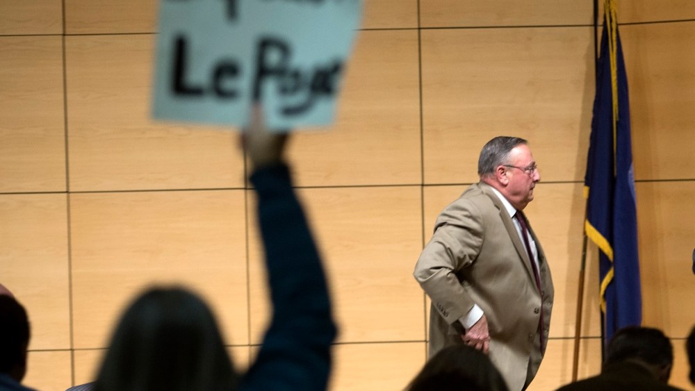 Gov. Paul LePage brings his town hall tour to Portland, speaking at the Abromson Center at the University of Southern Maine on Dec. 8, 2015. An audience member holds up a sign as LePage leaves the room. (Photo by Derek Davis/Portland Press Herald/Getty)
