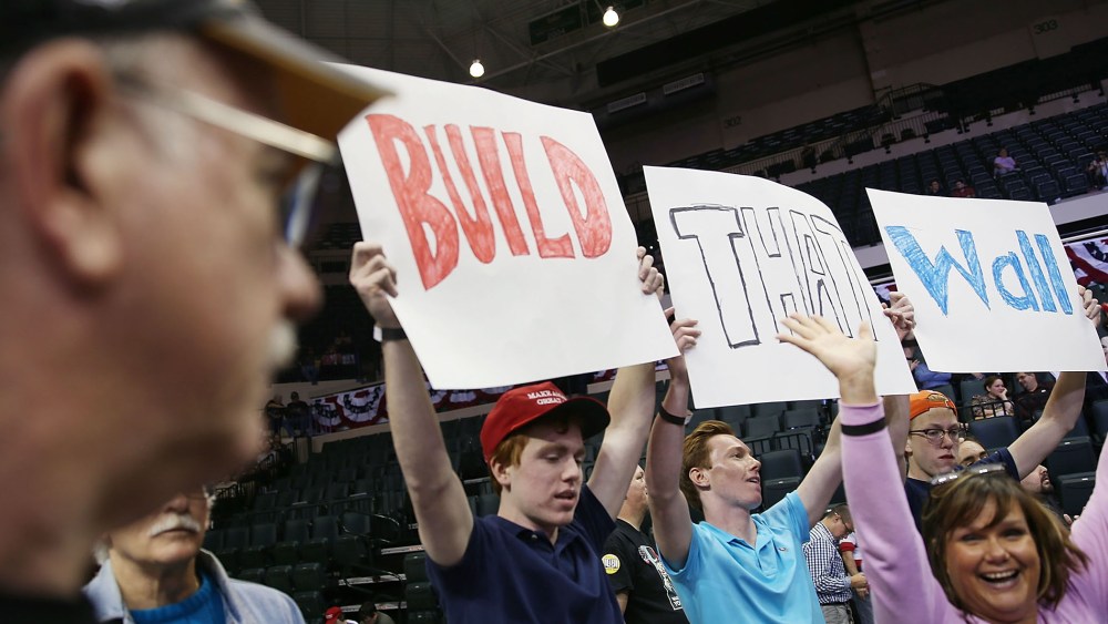 People hold signs that read, " Build that Wall", as they wait for the start of a campaign rally for Republican presidential candidate Donald Trump at the University of South Florida on Feb. 12, 2016 in Tampa, Fla. (Photo by Joe Raedle/Getty)