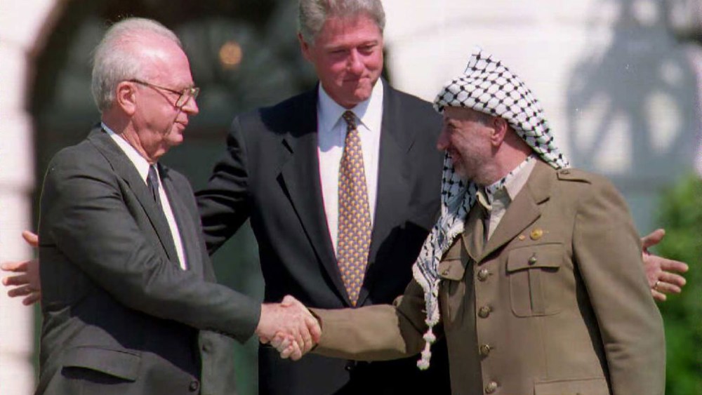 US President Bill Clinton stands between PLO leader Yasser Arafat and Israeli Prime Minister Yitzahk Rabin as they shake hands on Sep. 13, 1993 at the White House in Washington DC. (Photo by J. David Ake/AFP/Getty)
