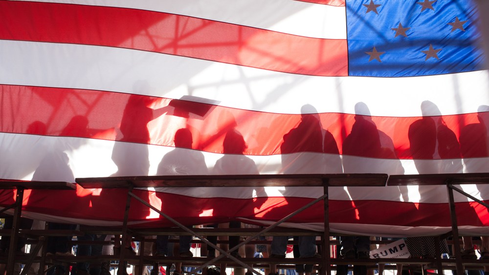 Supporters are seen backstage through an American flag during a Republican presidential candidate Donald Trump rally at the The Northwest Washington Fair and Event Center on May 7, 2016 in Lynden, Wash. (Photo by Matt Mills McKnight/Getty)