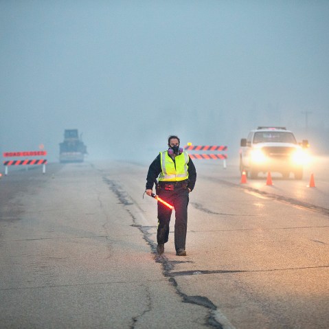 Smoke fills the air as a police officer stands guard at a roadblock along Highway 63 leading into Fort McMurray on May 8, 2016 near Fort McMurray, Alberta, Canada. (Photo by Scott Olson/Getty)