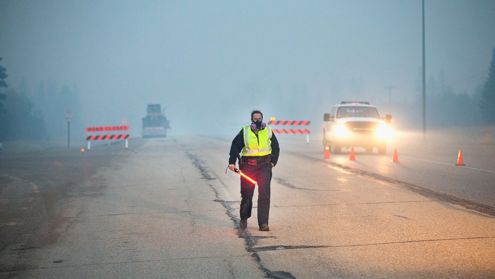Smoke fills the air as a police officer stands guard at a roadblock along Highway 63 leading into Fort McMurray on May 8, 2016 near Fort McMurray, Alberta, Canada. (Photo by Scott Olson/Getty)