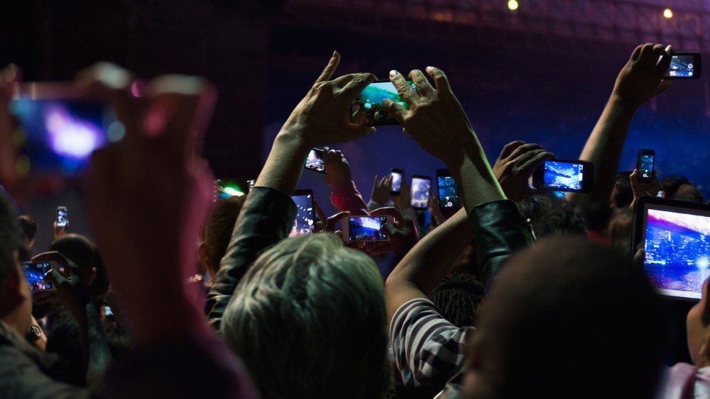 People in crowd take photos on their cell phones at night. (Photo by GS/Gallery Stock)