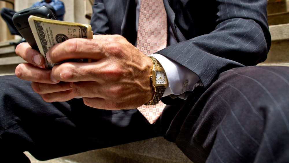 A businessman holding a cellphone and money in downtown Manhattan.