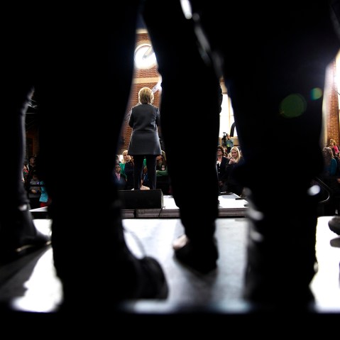 Seen through the legs of attendees, Hillary Clinton, a Democratic presidential hopeful, speaks during a campaign event at the Lyman and Merrie Wood Museum of Springfield History in Springfield, Mass.