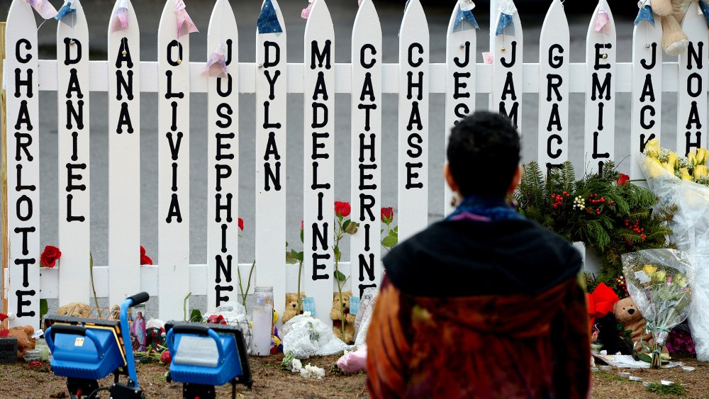 On Dec. 21, 2012 a woman kneels in front of a fence with the names of the 20 children killed in the school shooting at Sandy Hook Elementary School in Newtown, Conn.
