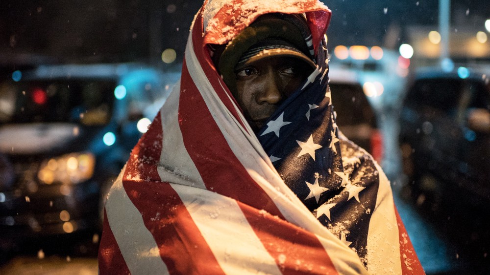 A protester covered in a U.S. flag stands in front of Ferguson Police Department as the snow falls, in Ferguson, Mo. on Nov. 26, 2014. (Photo by Alexey Furman/EPA)