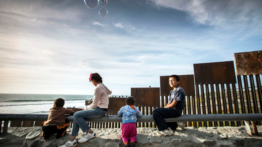 Children sit alongside the border fence beside the sea that divides Mexico from the United States, in Tijuana, Mexico.