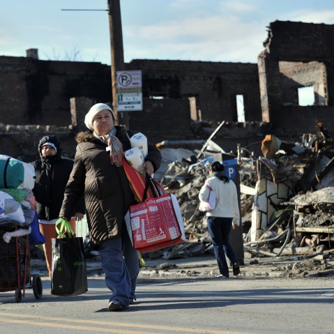 After getting household supplies from a nearby distribution center, people walk home past burned out businesses in the Rockaway Park section of Queens November 14, 2012 in New York as the city recovers from the effects of super storm Sandy. (AFP PHOTO...