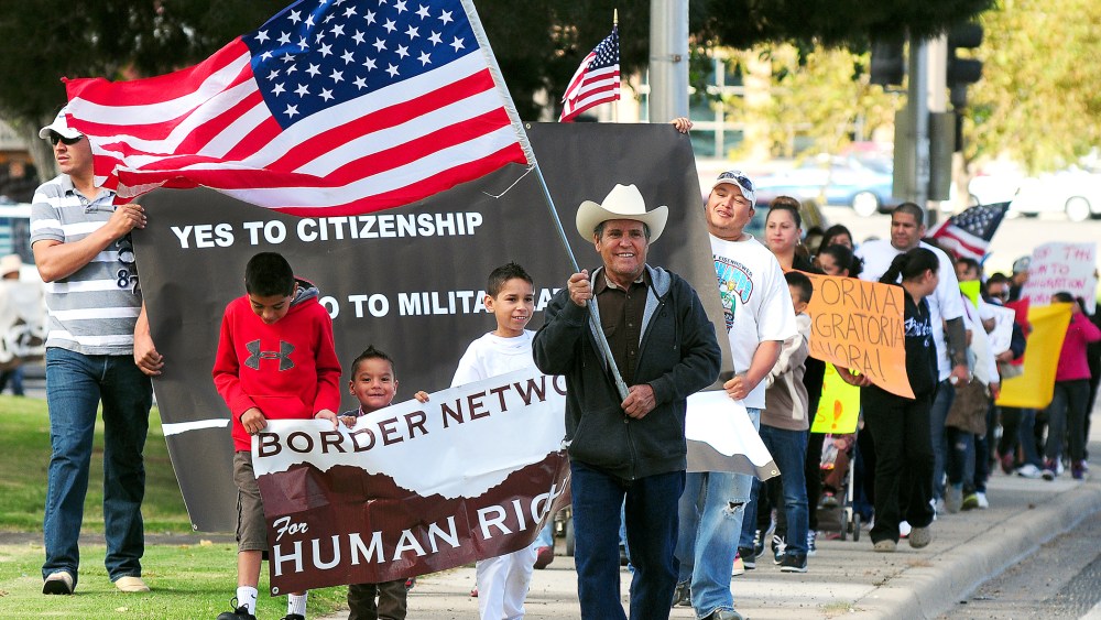 Jose Gonzalez of El Paso, Texas, center, carries the American flag as he leads Azriel Gutierrez, 11, left, Christian Flores, 3, Emiliano Cardona, 11, and hundreds of fellow marchers along Picacho Avenue in Las Cruces, N.M. on October 5, 2013 as they rally