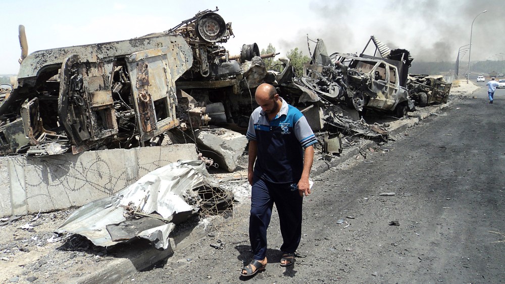 A man walks past near remains of burnt vehicles belonging to Iraqi security forces in the northern Iraq city of Mosul on June 13, 2014.