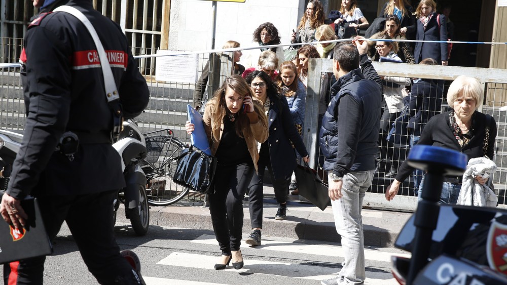 A plainclothes policeman helps to evacuate people from the tribunal building in Milan, Italy, after a shooting was reported inside a courtroom on April 9, 2015. (Photo by Luca Bruno/AP)