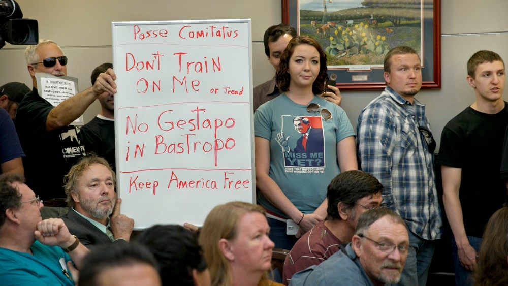 Bob Welch, standing at left, and Jim Dillon, hold a sign at a public hearing about the Jade Helm 15 military training exercise in Bastrop, Texas, Monday April 27, 2015.