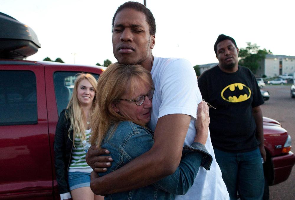 Judy Goos hugs her daughter's friend, Isaiah Bow, 20, while eye witnesses Emma Goos, 19, left, and Terrell Wallin, 20, right, gather outside Gateway High School where witnesses were brought for questioning early Friday morning in Denver.