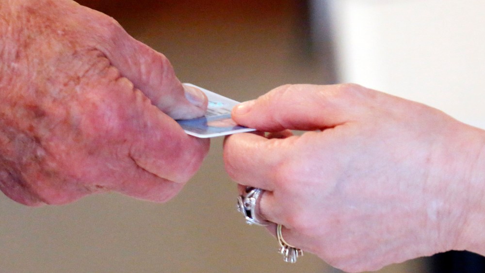 A Republican primary precinct worker hands back a voter's driver's license before handing over a voters access card in Madison, Miss., Tuesday, June 3, 2014.